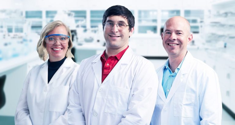 Olivia, Matt, and Mike posing in front of a lab wearing lab coats and glasses